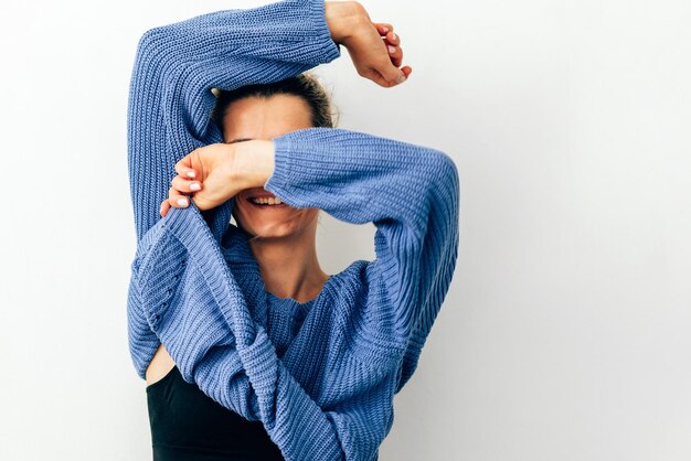 Photo playful smiling young woman pulling her blue trendy sweater over head having fun