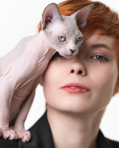 Playful Sphynx Cat standing on shoulder of redhead woman and gently pressed against her face