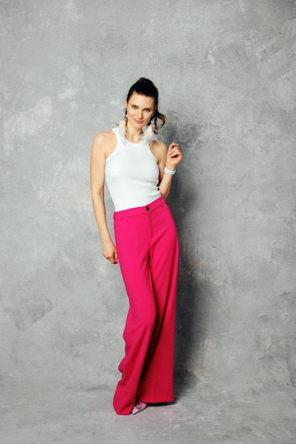 Playful woman in wide trousers and tank top posing on abstract grey background