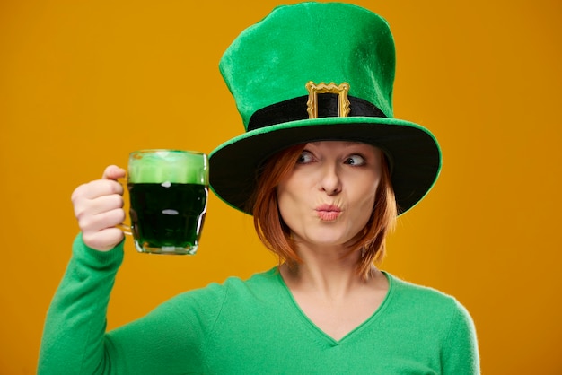 Donna giocosa con cappello da leprechaun che guarda la birra