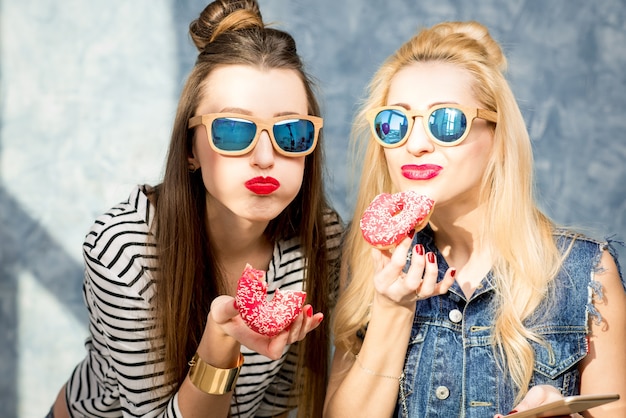 Playful women having fun with sweet donuts on the blue wall background