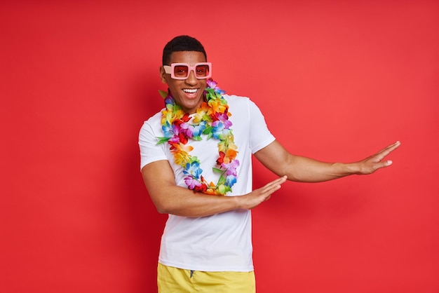 Photo playful young man in hawaiian necklace dancing against red background