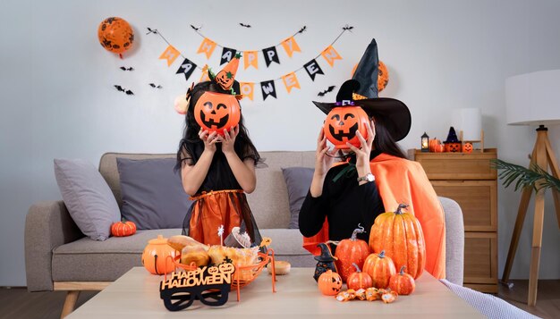 Playful young mother sitting on comfy couch in living room with cute little daughter tells spooky