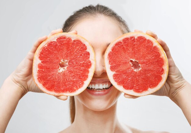 Playful young woman holding halves of citrus fruits against her eyes and smiling