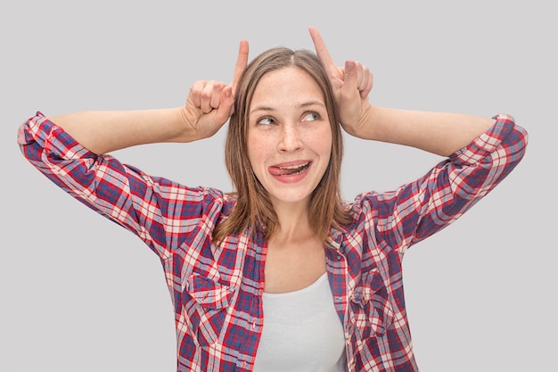 Playful young woman puts fingers on hands in horns position.