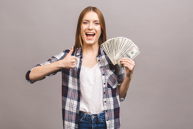 Playful young woman with long hair holding bunch of money banknotes and looking at camera. Thumbs up.