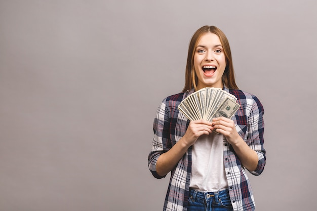 Playful young woman with long hair holding bunch of money banknotes and looking at camera