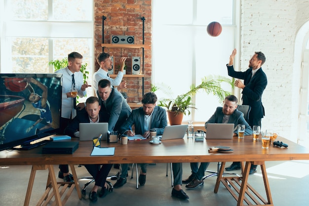 Playing basketball, screaming, laughting. Happy carefree colleagues having fun in office while their co-workers working hard and highly concentrated. Concept of fun, resting, professional occupation.