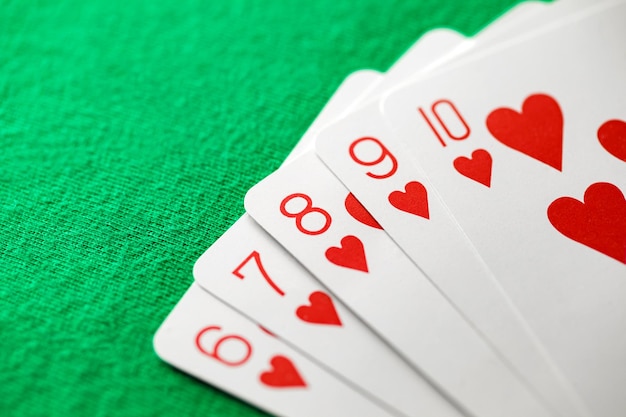 Playing cards poker combination straight flush red suit of hearts from six to ten on green background selective focus