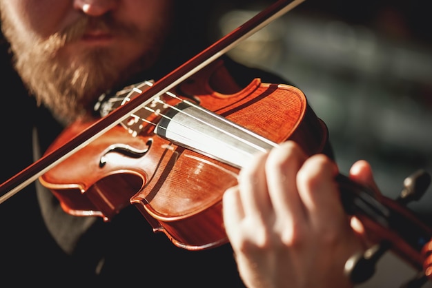 Playing classical music close up view of beard violinist playing classical music on the brown