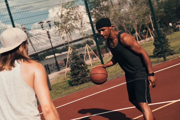 Playing fair. Two young men in sports clothing playing basketball while spending time outdoors