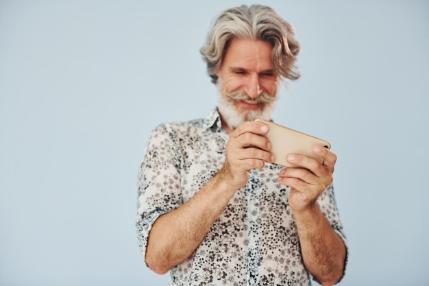 Playing game on phone Senior stylish modern man with grey hair and beard indoors