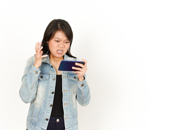 청바지 재킷과 검은 셔츠를 입은 아름다운 아시아 여성의 화난 얼굴로 전화로 게임하기