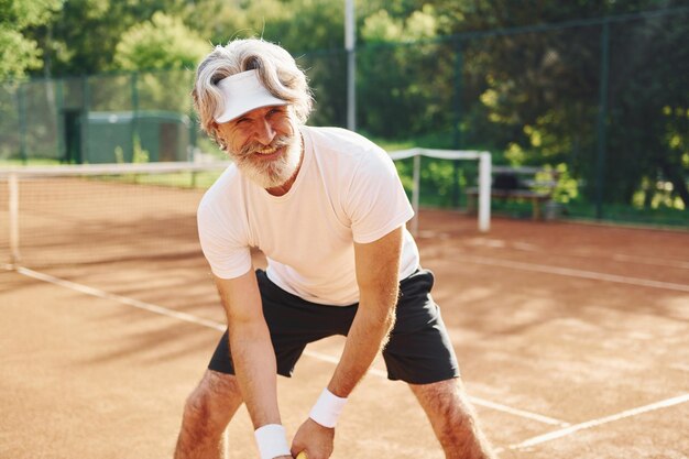 Playing game Senior modern stylish man with racket outdoors on tennis court at daytime