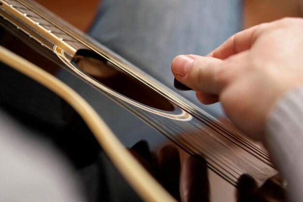 Playing the guitar Strumming black acoustic guitar Musician plays music Man fingers holding mediator Male hand playing guitar neck in dark room Unrecognizable person rehearsing fretboard closeup