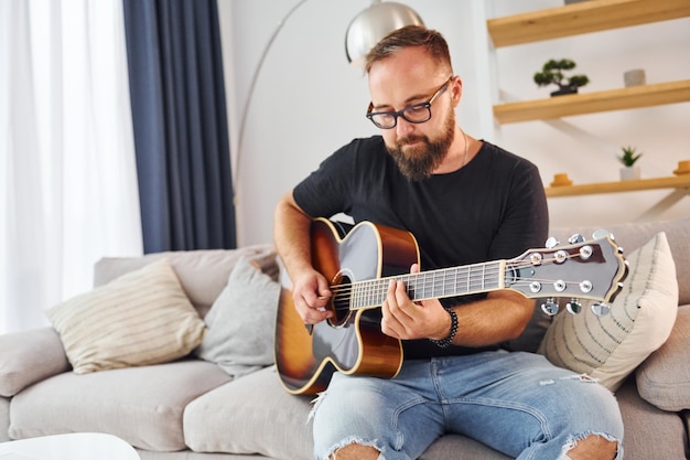 Playing the instrument Man in casual clothes and with acoustic guitar is indoors