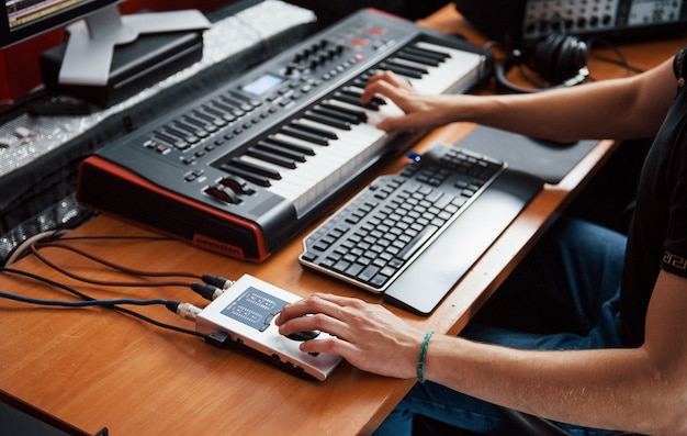 Playing midi keyboard. Sound engineer working and mixing music indoors in the studio.