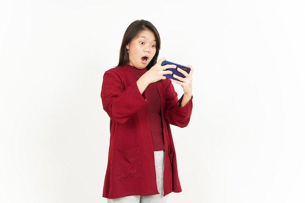 白で隔離赤いシャツを着て美しいアジアの女性のスマートフォンでモバイルゲームをプレイ