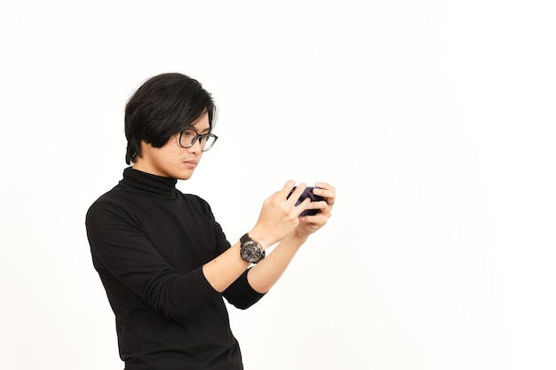 白い背景に分離されたハンサムなアジア人男性のスマート フォンでモバイル ゲームをプレイ