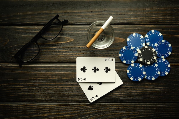 Играть в покер с выигрышной комбинацией одной пары карт с фишками и стаканами с сигаретой на черном винтажном столе в покерном клубе