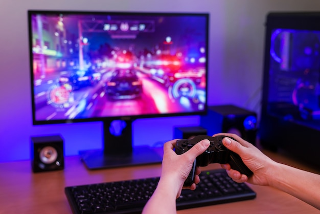 Photo playing racing games on computer concept. hand holds the joystick. in the background is a gaming computer with rgb light.