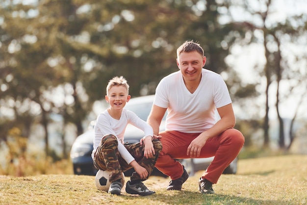 Playing soccer Father with his son spending weekend together outdoors near forest at daytime