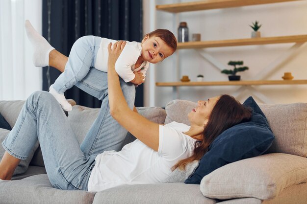 ソファーで遊んでいる母親と幼い娘が一緒に家にいる