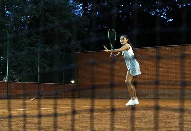 Playing tennis at night young girl blocking the ball with the tennis racket during the training