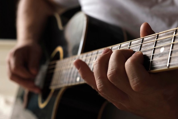 写真 ギターを弾く アコースティック ギターをかき鳴らす ミュージシャンが音楽を演奏する メディエーターを持つ男の指 暗い部屋でギターの首を弾く男の手 フレットボードのクローズ アップのリハーサルをしている人物