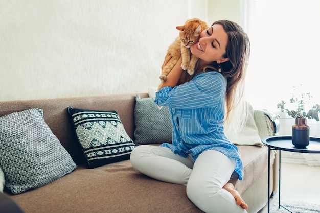 Playing with cat at home. Young woman sitting on couch with pet.