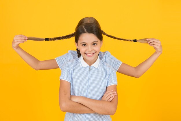 Playing with pigtails hair fashion beauty childhood happiness small girls in school uniform retro look children in vintage style old school kid fashion happy friends on yellow background