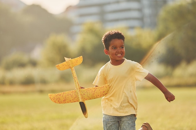 Photo playing with plane african american kid have fun in the field at summer daytime