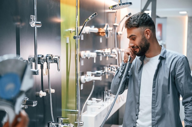 Playing with shower crane Pretending like talking by phone Stylish beautiul man is in the store of goods for the home