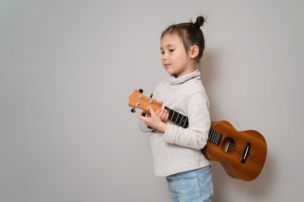 Plays the ukulele and sings early childhood development the\
girl has musical talent beautiful little girl practicing singing\
and playing the guitar