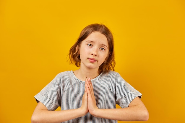 Молодая девушка на желтом фоне студии желает и молится, пожалуйста, язык жестов концепция позитивного образа жизни