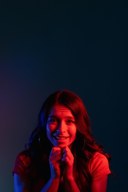 Pleading woman Asking apology Request favor Begging please Cute smiling young girl with imploring expression in bright red color neon light on dark copy space background