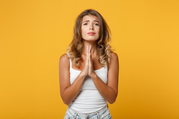 Pleading young woman girl in light casual clothes posing isolated on yellow orange background in studio. People sincere emotions lifestyle concept. Mock up copy space. Holding hands folded in prayer.