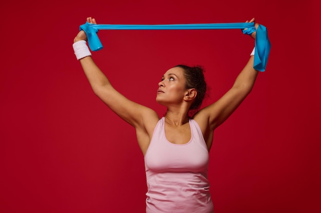 광고 복사 공간이 있는 빨간색 배경에 저항 고무 밴드로 체중 훈련을 하는 유쾌한 활동적인 여성