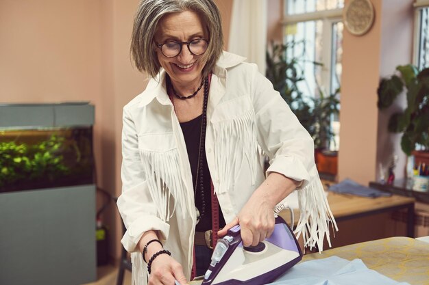 Foto la sarta sarta donna europea matura affascinante piacevole accarezza la camicia blu della nuova collezione in un laboratorio di cucito processo di cucito fashion design creazione di un nuovo capo in atelier di sartoria