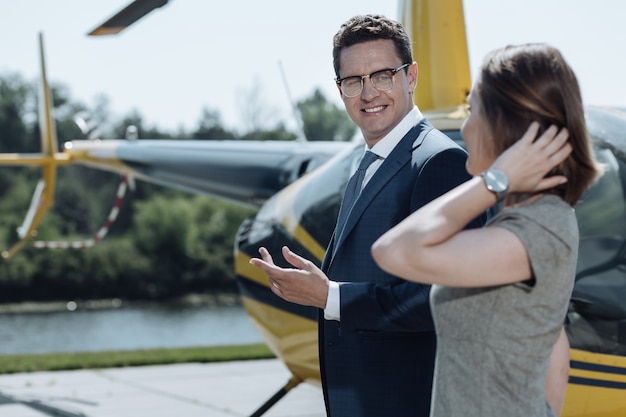 Pleasant communication. Charming young businessman talking to his colleague while being ready to take a helicopter flight together with her