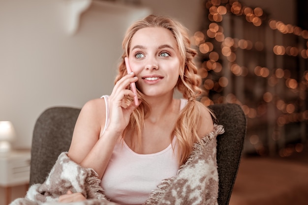 Pleasant face expression. Appealing light-haired woman with big blue eyes having conversation while relaxing in empty apartments