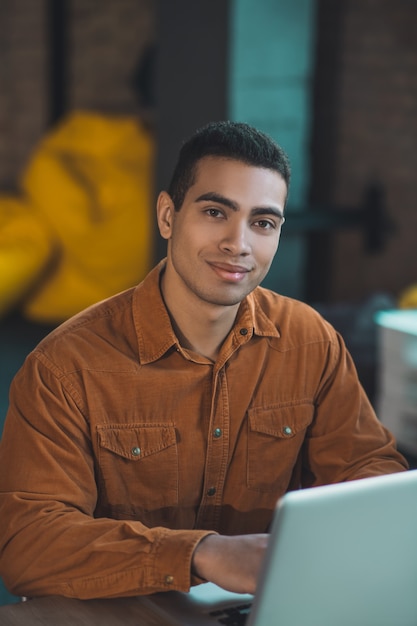 Photo pleasant good looking man smiling to you while sitting at his workplace