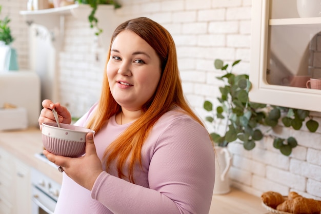 Pleasant good looking woman standing with a bowl while eating her food