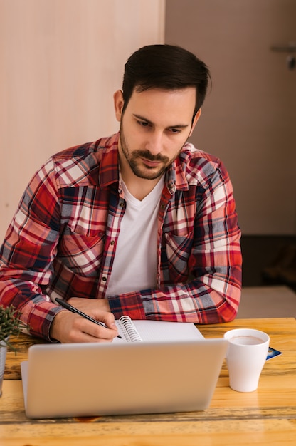 Photo pleasant handsome young guy sitting at the table and working