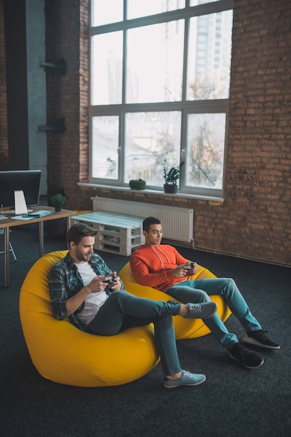 Pleasant happy men playing video games together while relaxing at home