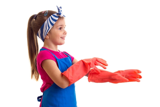 Pleasant little girl with ponytail wearing in pink shirt and blue apron with red gloves in studio