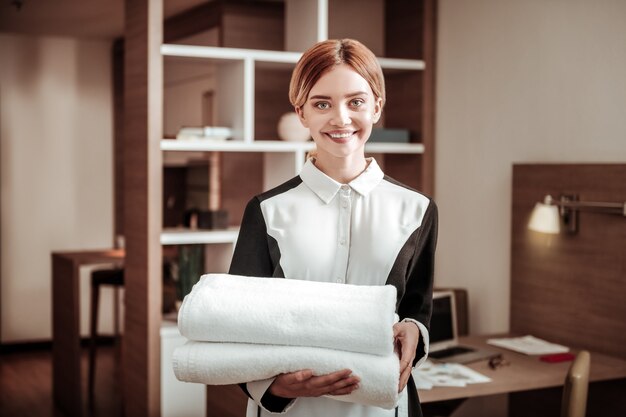 Pleasant maid. Young pleasant blonde-haired hotel maid holding white towels while working