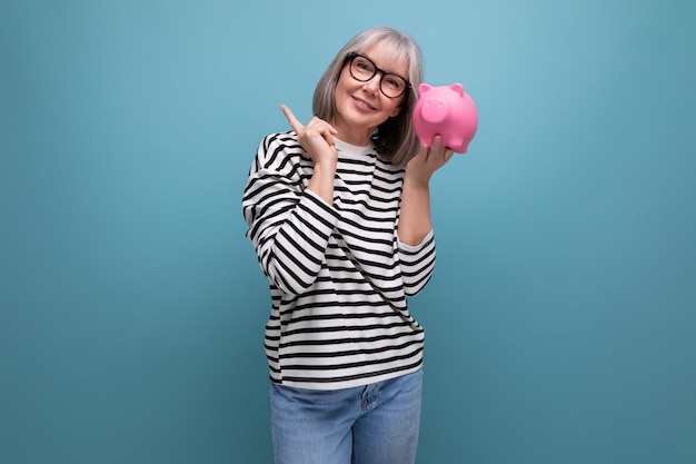 Pleasant middleaged woman years old holding a piggy bank with savings on a bright background with