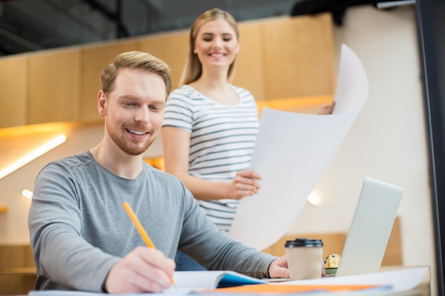 Piacevole bell'uomo bello sorridente e prendere appunti mentre si è al lavoro