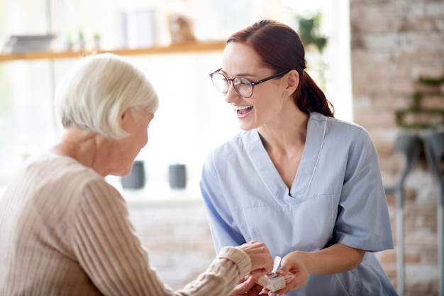 Photo pleasant nurse laughing while speaking with retired lady